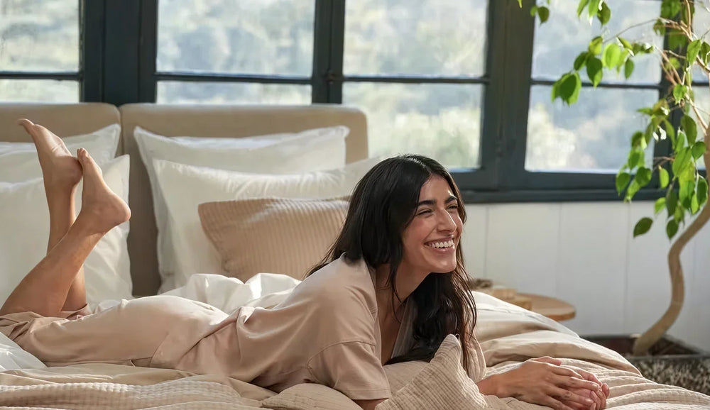 Woman lying on a bed in a cozy room with a plant and large windows.